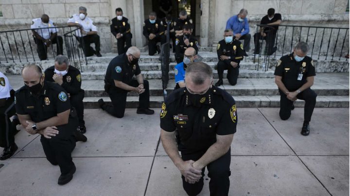 Manifestantes y oficiales de policía del condado de Miami-Dade arrodillados y rezando juntos.