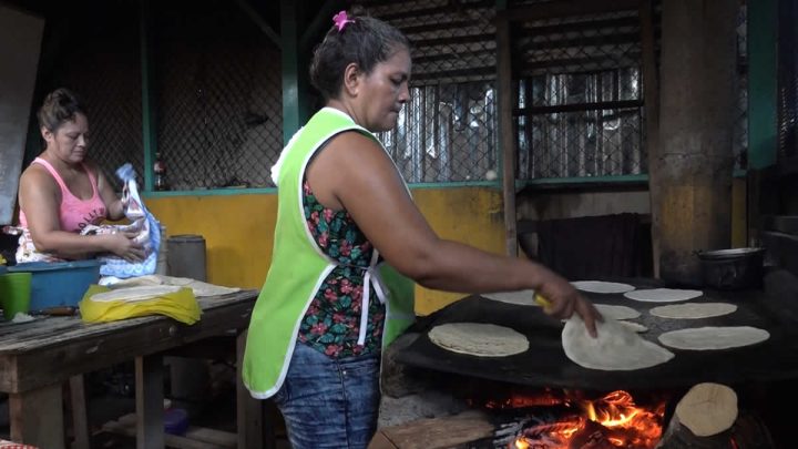 Mujer palmeando tortillas en comal.
